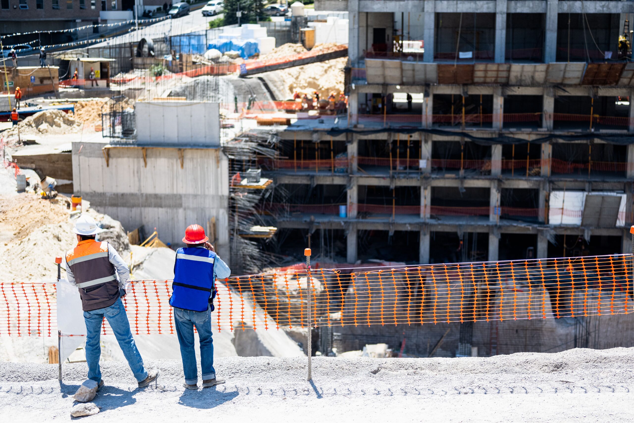 A high angle of two people with helmets standing in front of a construction site